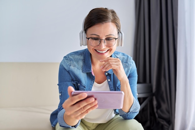 Femme d'âge moyen avec un casque et regardant l'écran du smartphone souriant parler