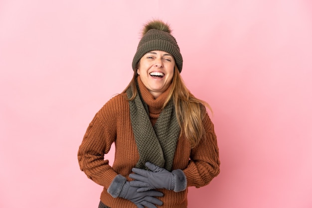 Femme d'âge moyen avec chapeau d'hiver isolé sur mur rose souriant beaucoup