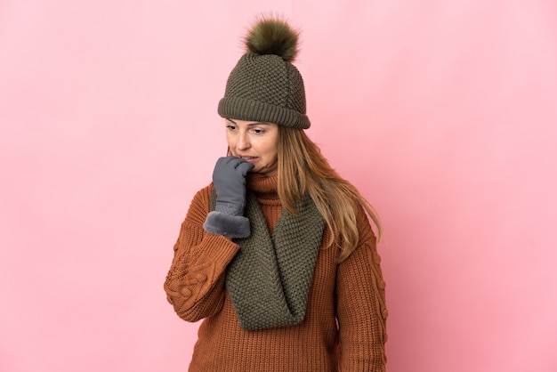 Femme d'âge moyen avec chapeau d'hiver isolé sur rose ayant des doutes