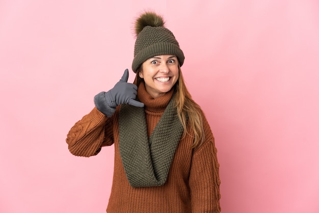 Femme d'âge moyen avec chapeau d'hiver isolé sur rose faisant le geste de téléphone. Rappelez-moi signe