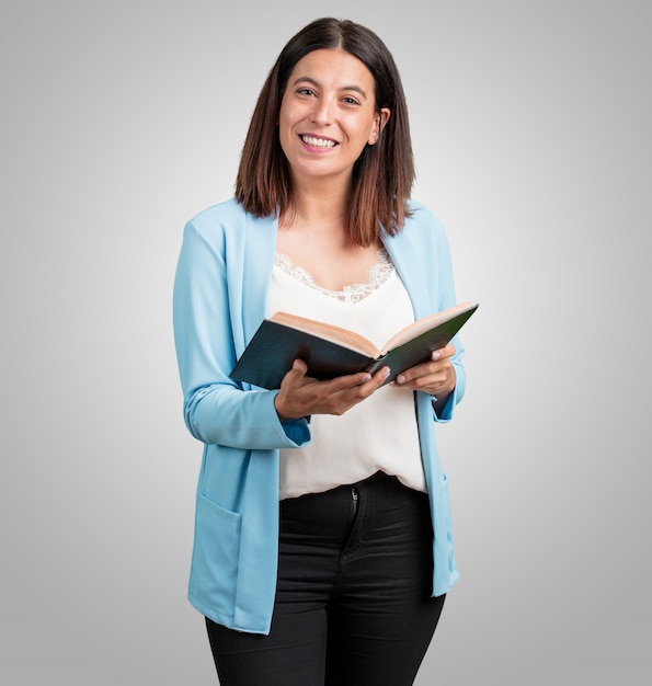 Femme d&#39;âge moyen concentré et souriant, tenant un manuel, étudiant pour passer un examen ou en lisant un livre intéressant