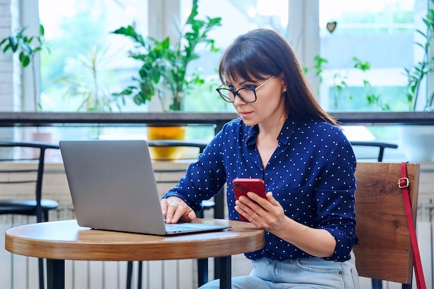 Une femme d'âge moyen dans un café avec un ordinateur portable.
