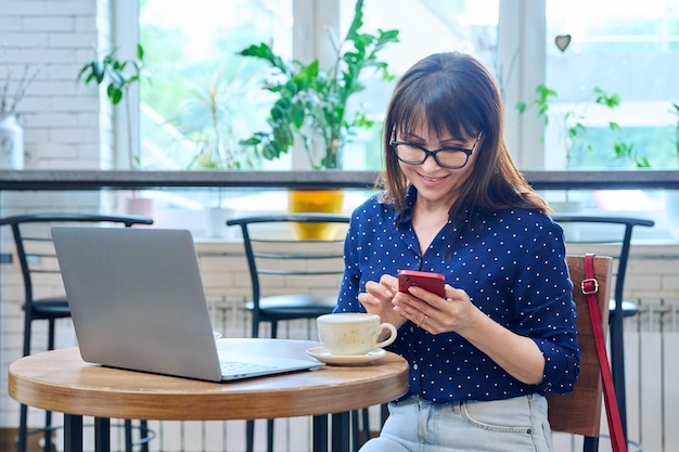 Une femme d'âge moyen dans un café avec un ordinateur portable.