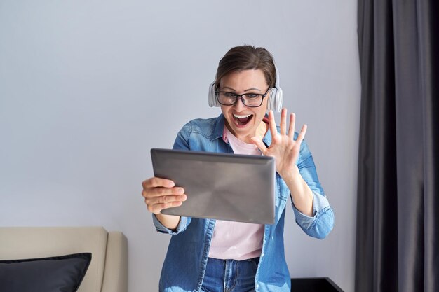 Femme d'âge moyen dans un casque avec tablette numérique à la maison sur un fauteuil