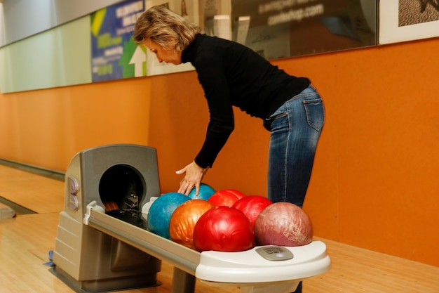 Une femme d'âge moyen dans un club de bowling choisit des balles de bowling