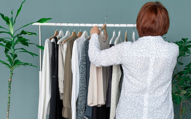 Une femme d'âge moyen fait du shopping et regarde la nouvelle robe près de l'étagère avec des vêtements.