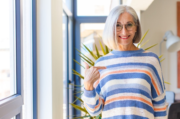 Femme d'âge moyen à la fierté, confiante et heureuse, souriante et pointant vers soi ou faisant signe numéro un