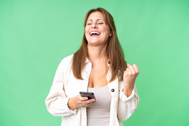 Femme d'âge moyen sur fond isolé avec téléphone en position de victoire