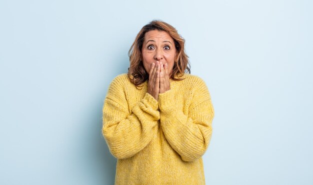 Femme d'âge moyen heureuse et excitée, surprise et étonnée couvrant la bouche avec les mains, riant avec une expression mignonne