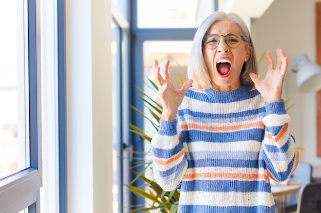 Photo femme d'âge moyen hurlant furieusement, se sentant stressée et agacée avec les mains en l'air en disant pourquoi moi