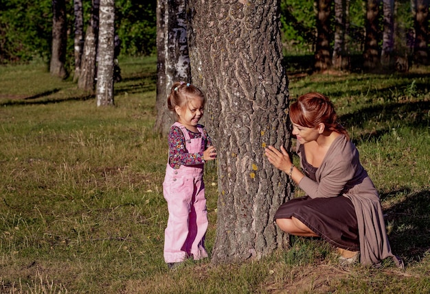 Femme d'âge moyen jouant avec une petite fille se cachant derrière un arbre en été