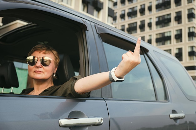 Femme d'âge moyen avec des lunettes de soleil au volant d'une voiture montrant le doigt du milieu