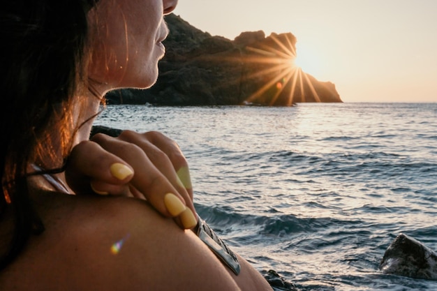 Femme d'âge moyen en maillot de bain blanc et braclets de style bohème pratiquant à l'extérieur sur un tapis de yoga au bord de la mer au coucher du soleil Routine de fitness yoga pour femmes Harmonie et méditation d'un mode de vie sain