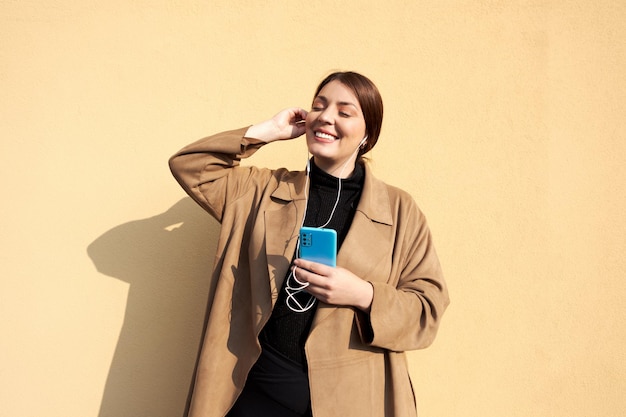 Photo femme d'âge moyen en manteau marron écoutant de la musique sur un téléphone bleu