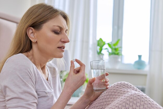 Femme d'âge moyen mature à la maison au lit tenant la pilule et un verre d'eau douce