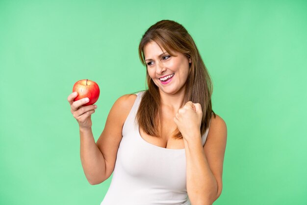 Femme d'âge moyen avec une pomme sur fond isolé célébrant une victoire