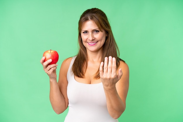 Femme d'âge moyen avec une pomme sur fond isolé invitant à venir avec la main Heureux que vous soyez venu