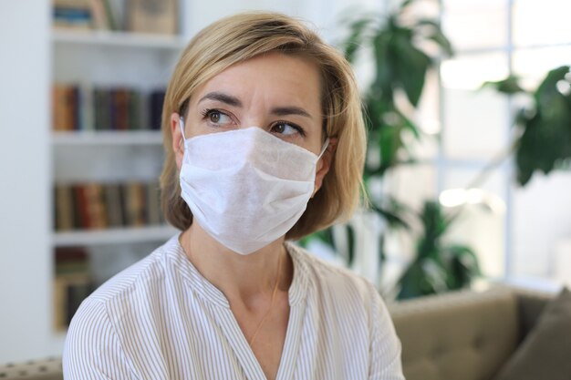 Femme d'âge moyen portant un masque médical à la maison pendant une situation épidémique.