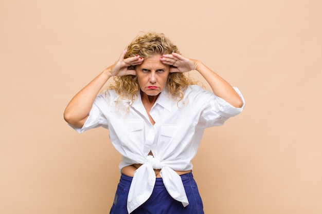 Femme d'âge moyen à la recherche concentrée, réfléchie et inspirée, remue-méninges et imaginant avec les mains sur le front