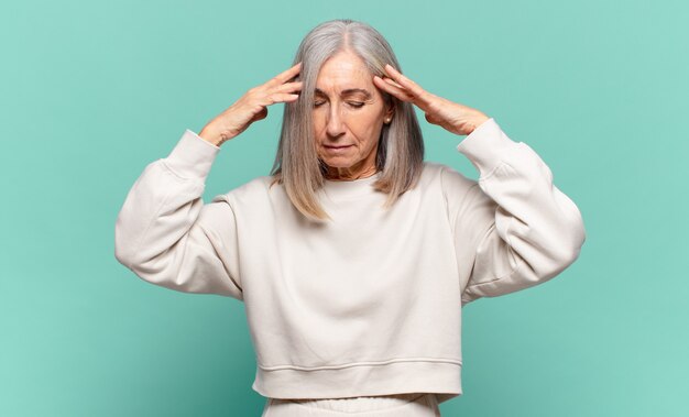 Femme d'âge moyen à la recherche concentrée, réfléchie et inspirée, remue-méninges et imaginant avec les mains sur le front