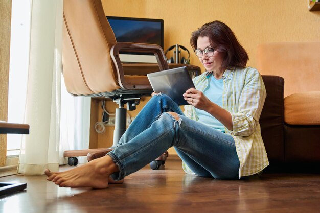 Femme d'âge moyen regardant le lieu de travail d'une tablette numérique avec fond d'ordinateur