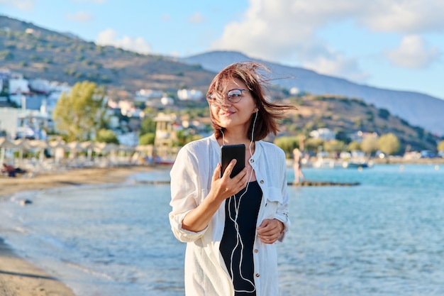 Femme d'âge moyen relaxante sur la plage portant des écouteurs avec smartphone