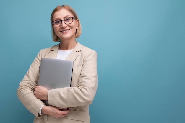 Femme d'âge moyen réussie en veste avec ordinateur portable pour travailler sur fond de studio avec espace de copie