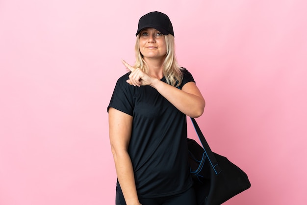 Femme d'âge moyen avec sac de sport isolé sur mur rose pointant vers le côté pour présenter un produit