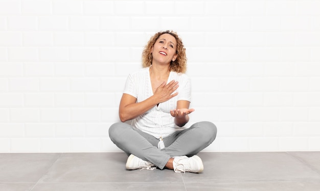 Femme d'âge moyen se sentant heureuse et amoureuse, souriant d'une main à côté du cœur et de l'autre tendue à l'avant