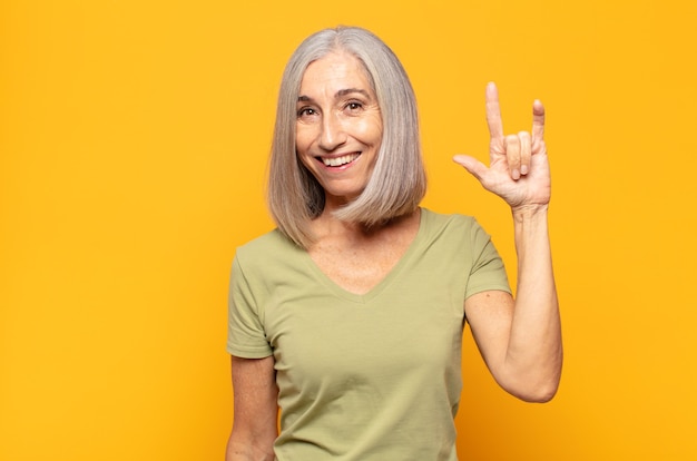 Femme d'âge moyen se sentant heureuse, amusante, confiante, positive et rebelle, faisant du rock ou du heavy metal signe avec la main