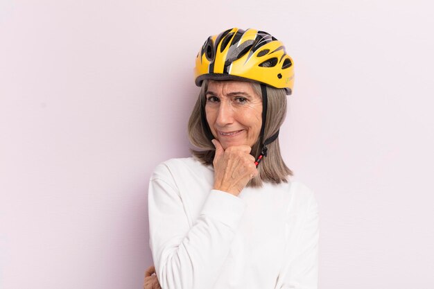 Femme d'âge moyen souriant avec une expression confiante heureuse avec la main sur le concept de casque de vélo de menton