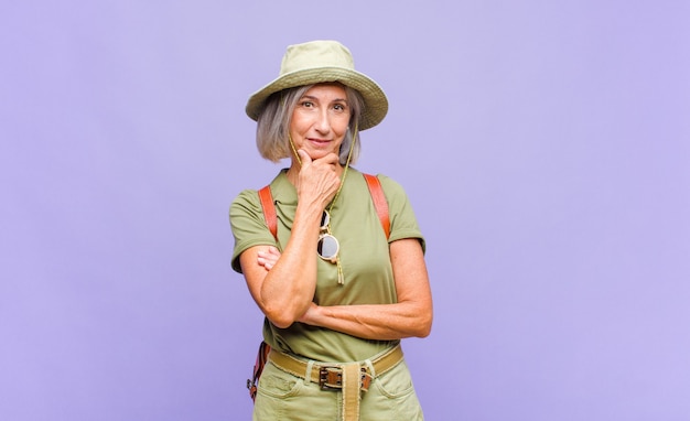 Femme d'âge moyen souriant avec une expression heureuse et confiante avec la main sur le menton, se demandant et regardant sur le côté