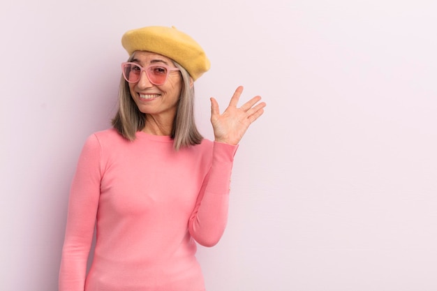 Femme d'âge moyen souriant joyeusement en agitant la main vous accueillant et vous saluant