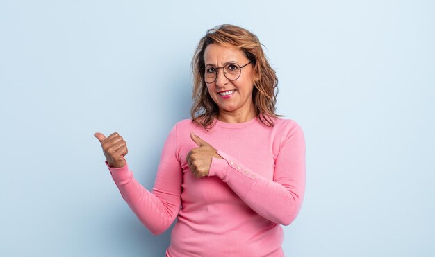 Femme d'âge moyen souriant joyeusement et avec désinvolture pointant vers l'espace de copie sur le côté, se sentant heureuse et satisfaite