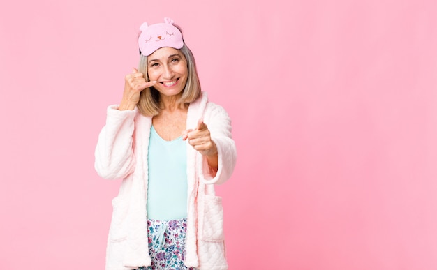 Femme d'âge moyen souriant joyeusement et pointant tout en vous appelant plus tard, en parlant au téléphone. concept de costume de nuit