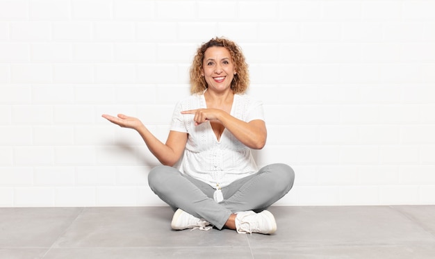 Femme d'âge moyen souriant joyeusement et pointant vers l'espace de copie sur la paume sur le côté, montrant ou annonçant un objet