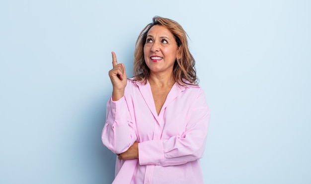 Femme d'âge moyen souriant joyeusement et regardant de côté, se demandant, pensant ou ayant une idée