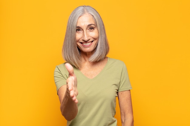 Femme d'âge moyen souriant, à la recherche de plaisir, confiant et sympathique, offrant une poignée de main pour conclure un accord, coopérant