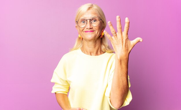 Femme d'âge moyen souriant et à la sympathique, montrant le numéro cinq ou cinquième avec la main vers l'avant, compte à rebours