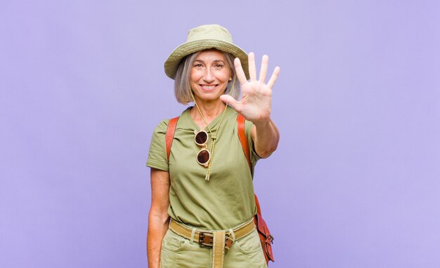 Femme d'âge moyen souriant et à la sympathique, montrant le numéro cinq ou cinquième avec la main vers l'avant, compte à rebours