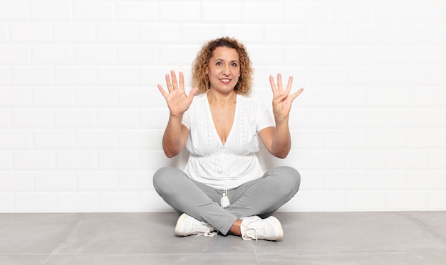 Photo femme d'âge moyen souriant et à la sympathique, montrant le numéro neuf ou neuvième avec la main en avant, compte à rebours