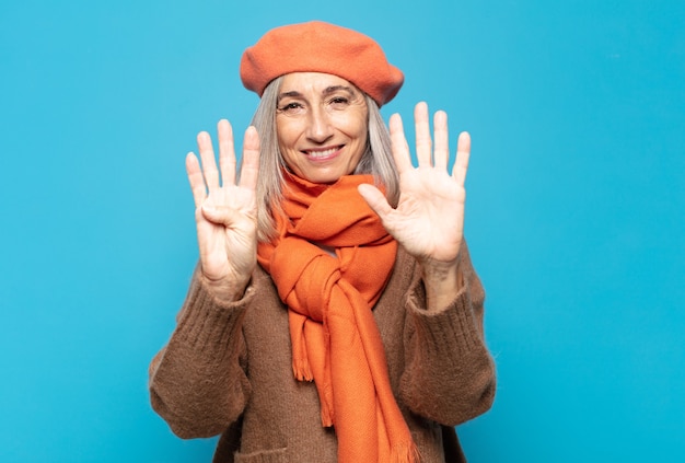 Femme d'âge moyen souriant et à la sympathique, montrant le numéro neuf ou neuvième avec la main en avant, compte à rebours