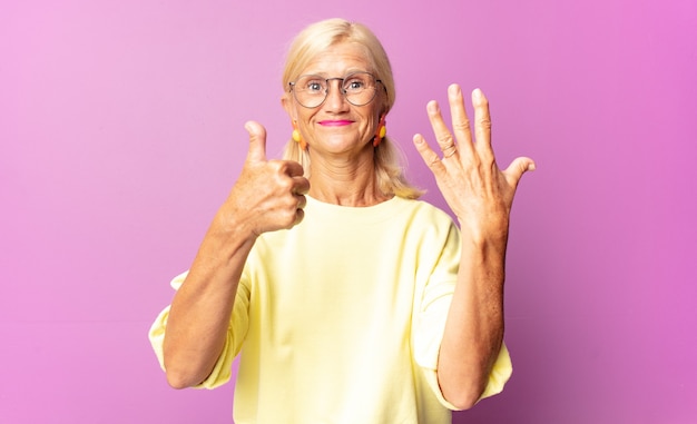 Femme d'âge moyen souriant et à la sympathique, montrant le numéro six ou sixième avec la main en avant, compte à rebours