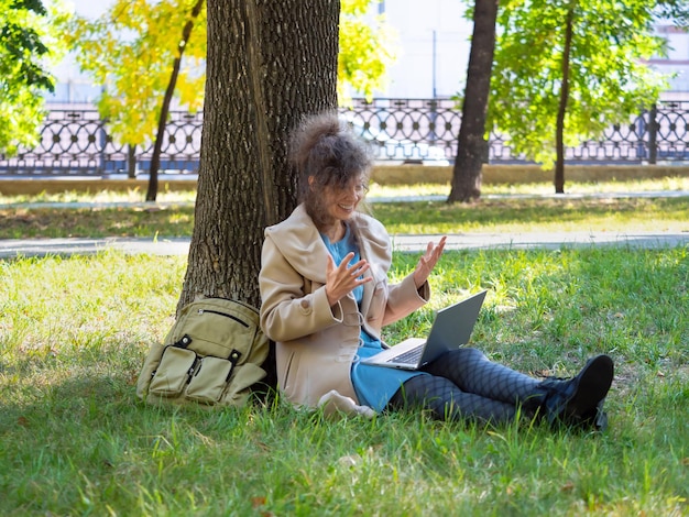 Femme d'âge moyen souriante avec ordinateur portable dans l'appel vidéo en ligne du parc de la ville