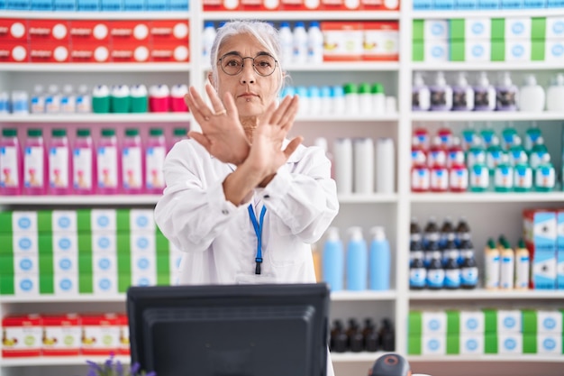 Femme d'âge moyen avec des tatouages travaillant à la pharmacie pharmacie expression de rejet croisant les bras et les paumes faisant un signe négatif visage en colère