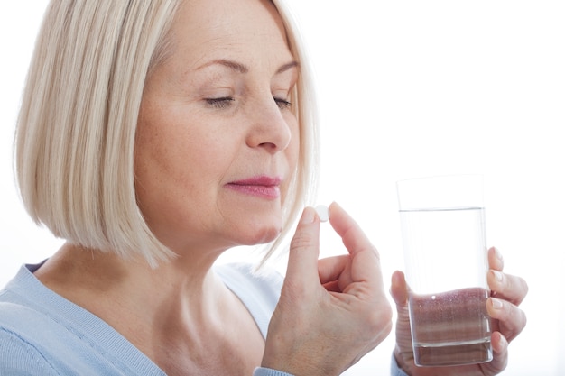 femme d'âge moyen tenant une pilule et un verre d'eau