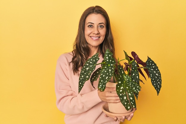 Femme d'âge moyen tenant une plante sur fond de studio jaune