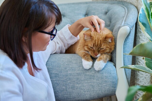 Photo femme d'âge moyen touchant le fond intérieur de la maison du chat de compagnie au gingembre