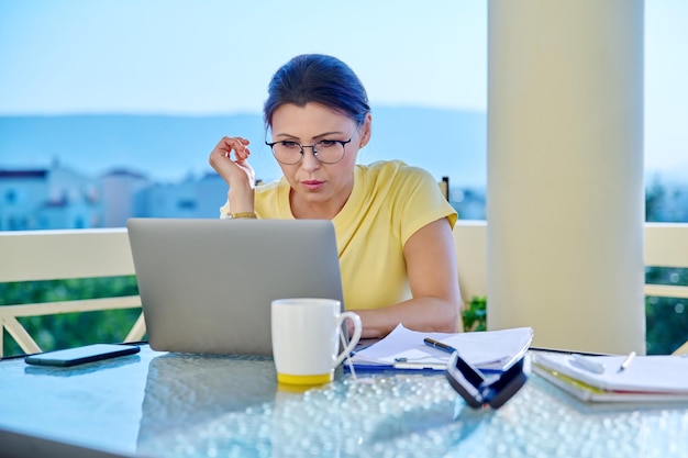 Femme d'âge moyen travaillant dans un bureau à domicile sur une terrasse