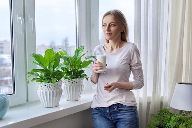 Femme d'âge moyen avec un verre de lait à la maison près de la fenêtre